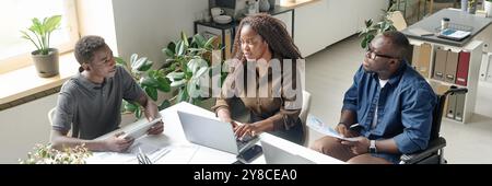 Website banner of young African American team of developers sitting at white table with laptops and having business meeting Stock Photo