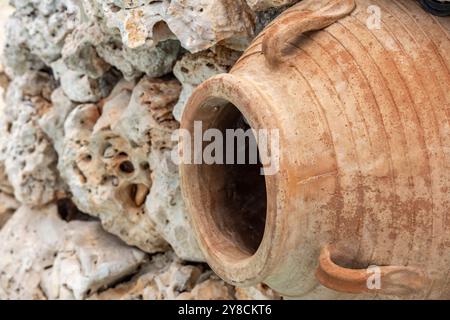 large terracotta wine or olive jar on its side set into a rockery in a garden as decoration or garden water feature. Stock Photo