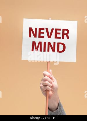male hand holding a white sign with phrase NEVER MIND in bold red letters. against orange background Stock Photo
