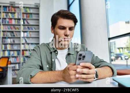 A focused student studies intently while using his smartphone in a vibrant library setting. Stock Photo