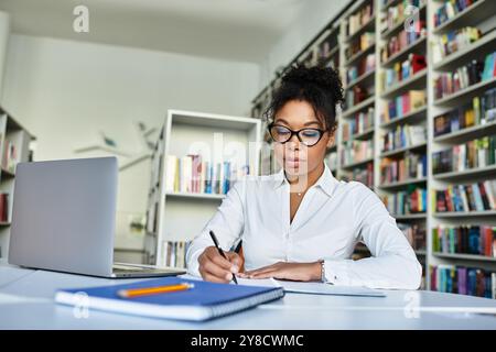 A dedicated African American teacher outlines plans at a desk surrounded by bookshelves. Stock Photo