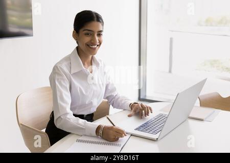 Young Indian businesswoman work online using laptop take notes Stock Photo