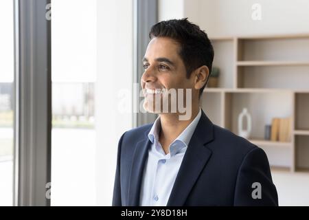 Happy young Indian man in formal suit look at window Stock Photo