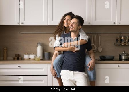 Happy dreamy wife sitting on kitchen counter, embracing husband Stock Photo