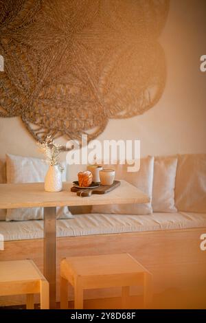 Cozy café table setup with two ceramic coffee mugs, a pastry, a white vase with dried flowers, and a magazine, bathed in warm natural light. Stock Photo