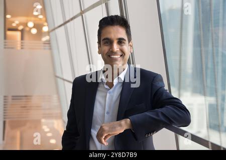 Happy successful Indian businessman leaning on rail at window Stock Photo