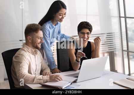 Three cheerful multiethnic business colleagues using laptop together Stock Photo