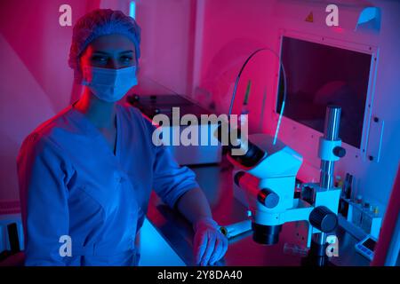 Scientist standing by a microscope in a brightly lit lab Stock Photo