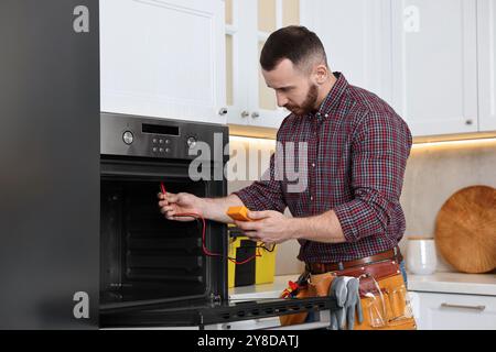 Repairman testing oven element with multimeter in kitchen Stock Photo