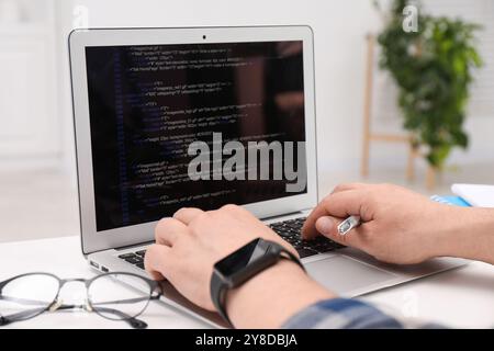 Programmer working with laptop at white desk in office, closeup Stock Photo