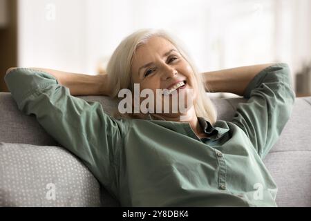 Carefree mature female leaned on sofa relaxing at home Stock Photo