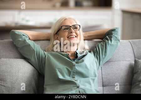 Satisfied older woman resting leaned on soft couch Stock Photo