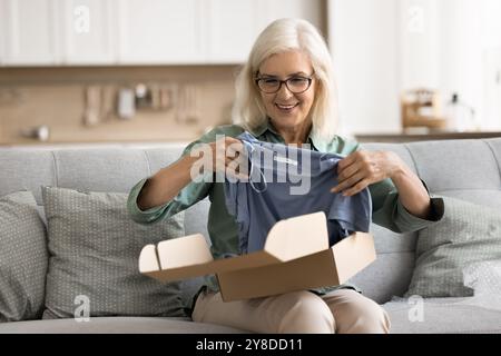 Happy older woman opening parcel box with bought fashion apparel Stock Photo
