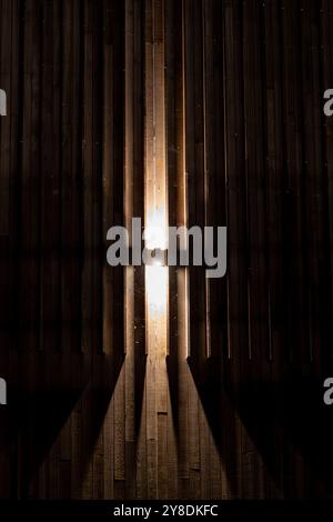 A wooden wall with vertical planks illuminated by a central light source, creating a cross-shaped shadow pattern. Stock Photo