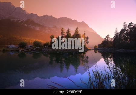 Idyllic lake at sunrise, a picturesque scenery with majestic mountains and the golden sunlight coming in behind the trees, dramatic colors Stock Photo