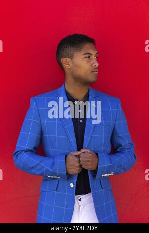 Attractive african american businessman in stylish suit is fastens his jacket and smiling, red background. Vertical portrait Stock Photo
