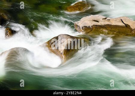 Fresh river water crashing swirling and spraying on tubulent journey around large rocks Stock Photo