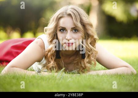Top view of attractive female model lying on green grass in park and looking at camera during time for taking rest, portrait of Caucasian woman with b Stock Photo