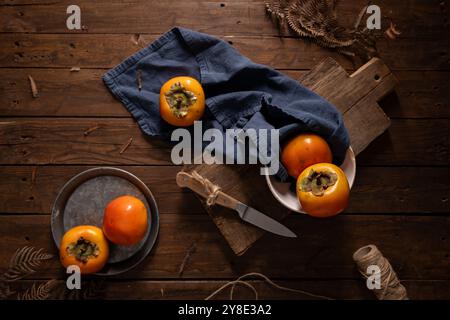 Ripe persimmons on a rustic wooden table, with a blue cloth and a cutting board. Stock Photo