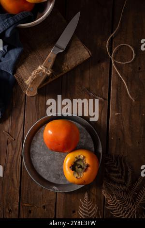 Rustic still life of persimmons on a metal plate with a wooden backdrop Stock Photo