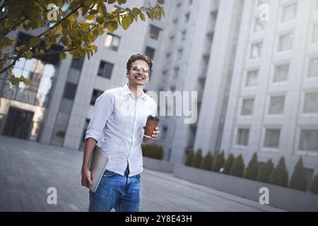 Cheerful young handsome well dressed man holding laptop computer and cup of coffee Stock Photo