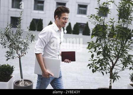 Cheerful young handsome well dressed man holding laptop computer and cup of coffee Stock Photo