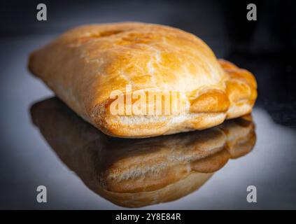 Close-up of the pastry of the fresh,cold pasty snack,ready to prepare and eat,simply placed,isolated on a shiny black surface,before cutting or adding Stock Photo