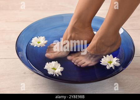 Woman soaking her feet in bowl with water and flowers on floor, closeup. Body care Stock Photo