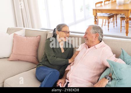 Happy senior diverse couple sitting on sofa and smiling Stock Photo