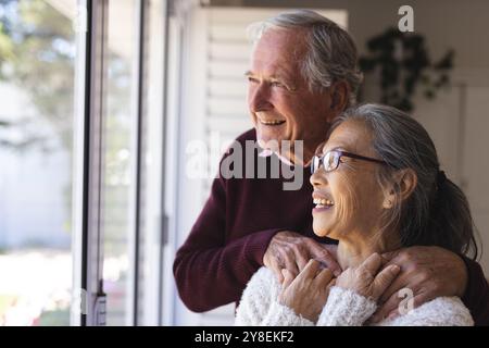 Happy senior diverse couple embracing and looking through window Stock Photo