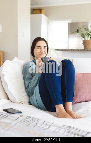 Smiling caucasian young woman with coffee mug contemplating and looking away while sitting on sofa Stock Photo