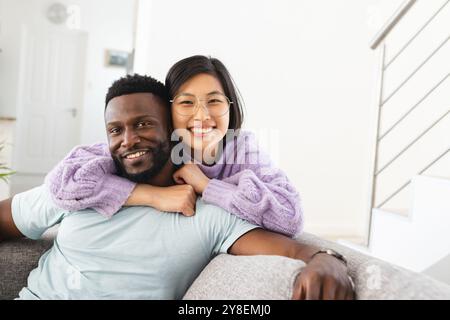 Portrait of happy diverse couple sitting on sofa and embracing Stock Photo