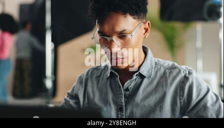 Man, photographer and glasses with laptop for production, film making or design at studio. Young, male person or producer working on computer for Stock Photo