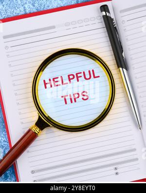 Helpful Tips words in an open notebook through a magnifying glass, top view. Stock Photo