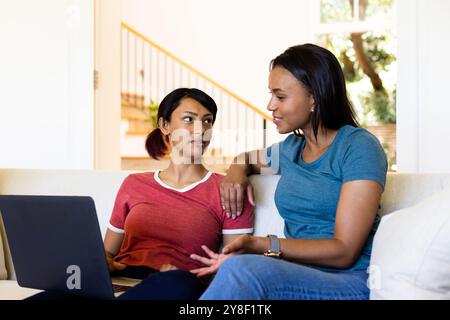 Happy biracial sisters sitting on couch and using laptop Stock Photo