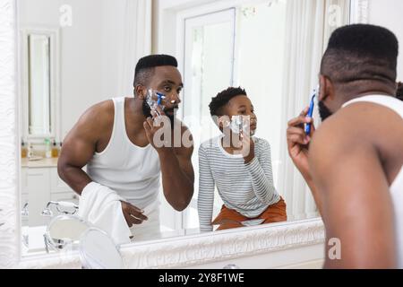 Happy african american father and son shaving beard in bathroom Stock Photo