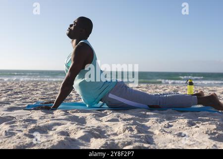 Relaxed african american man exercising outdoors, practicing yoga on beach Stock Photo