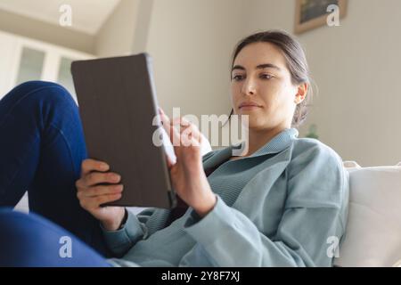 Beautiful caucasian young woman using digital tablet while sitting on sofa at home, copy space Stock Photo