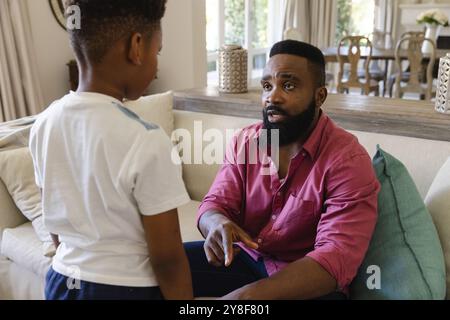 African american father sitting on sofa in living room, disciplining his son Stock Photo