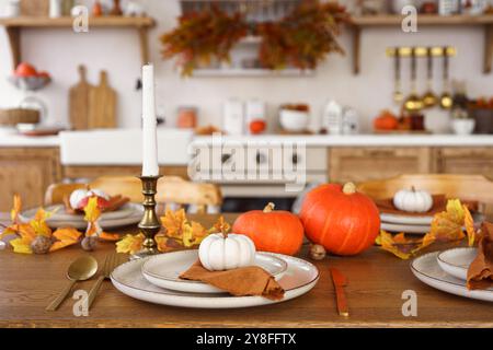 Dinning table is set for dinner with white and orange pumpkins, fall leaves, and candlestick on kitchen  background. Home decor for Halloween, Thanksg Stock Photo