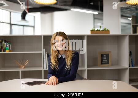 Portrait of a young Caucasian woman sitting at a table with a tablet computer, smiling in the modern office of a creative business Stock Photo