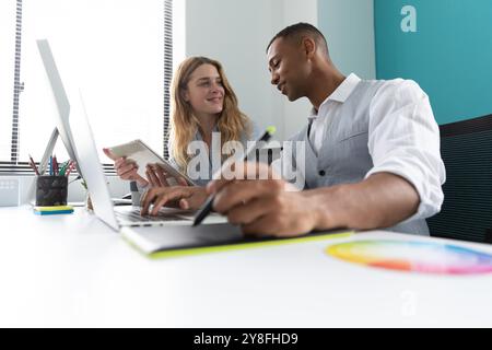 Side view close up of a young African American man using a laptop computer and a graphics tablet and a young Caucasian woman holding a tablet computer Stock Photo