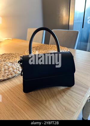 Stylish fashion black handbag placed elegantly on a wooden table. Soft lighting creates a warm atmosphere, highlighting the design and texture of the Stock Photo