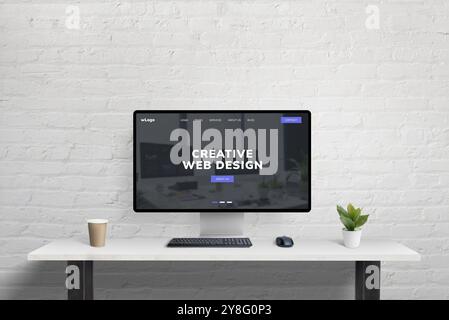 Clean creative web design page from code studio displayed on a computer at a tidy office desk with coffee and plant, set against a brick wall backgrou Stock Photo