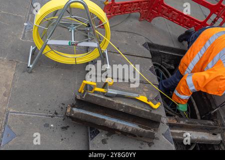 A technician in the field of telephony or communication inserts new cables in a hole in the street to fix some problem Stock Photo