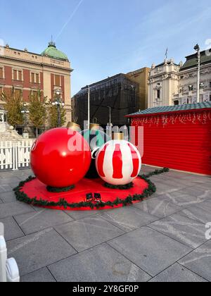 Colorful giant Christmas ornaments displayed in city square, adding a festive touch to the urban landscape. Holiday spirit amidst historic and modern Stock Photo