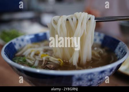 Vietnamese rice noodles in a bowl with chopsticks on a wooden table Stock Photo