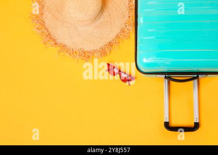 Turquoise suitcase, straw hat and sunglasses on yellow background, flat lay. Space for text Stock Photo