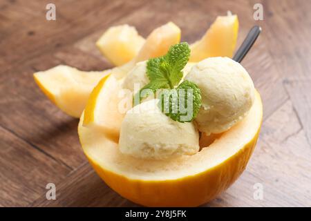 Scoops of tasty melon sorbet with mint in fresh fruit on wooden table, closeup Stock Photo