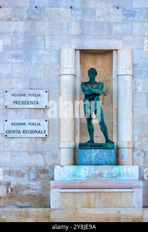 The statue depicted is "Il Costruttore," located on the facade of the building of the Presidenza della Regione Puglia in Bari, Italy. Stock Photo